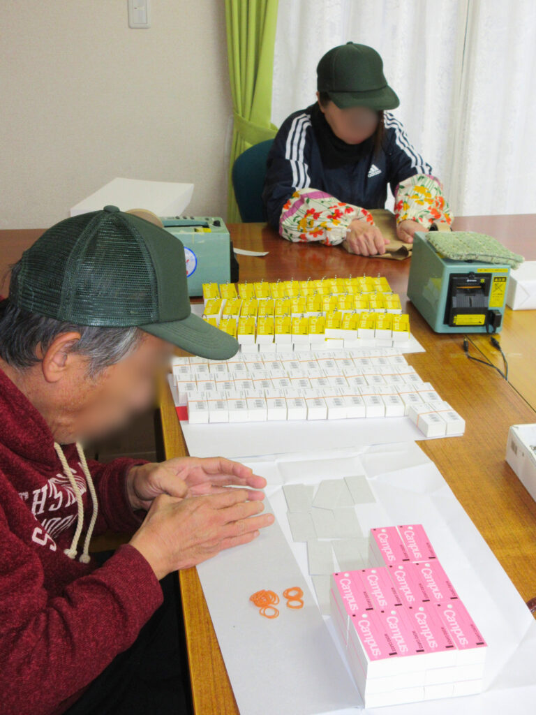 写真。二人ので封入作業をする様子。