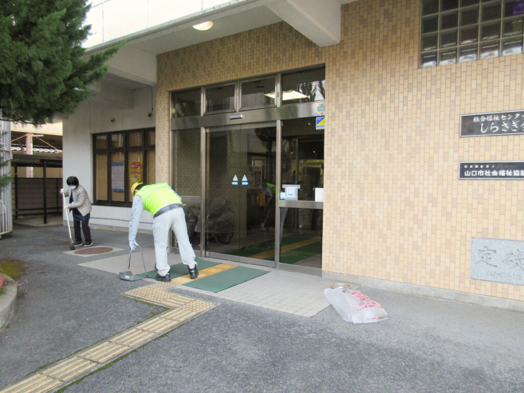 写真。しらさぎ会館の玄関前を清掃を行なっている。